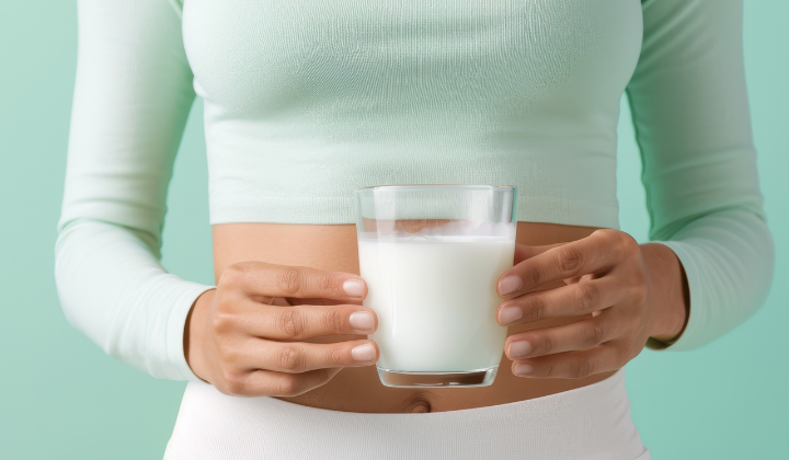 Intolérance au lactose Une femme avec un haut turquoise et un pantalon blanc tient un verre de lait des deux mains.