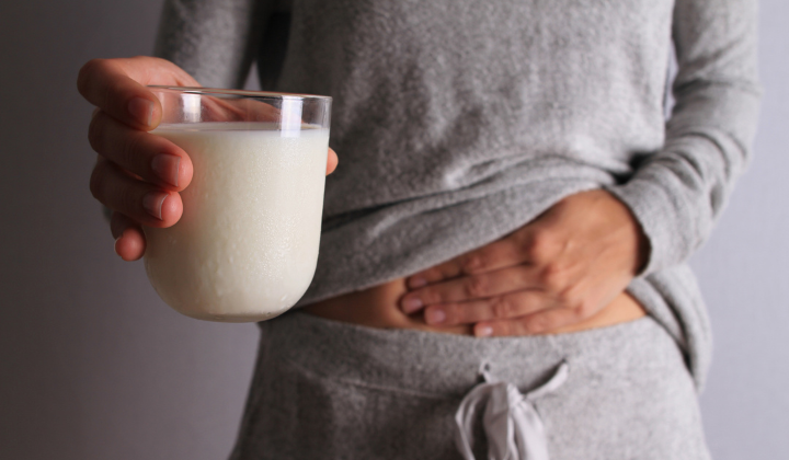 Lactose et lactase Une femme porte une tenue d'entraînement grise et confortable et tient son ventre de la main droite en signe de douleur. De la main gauche, elle tient un verre de lait.
